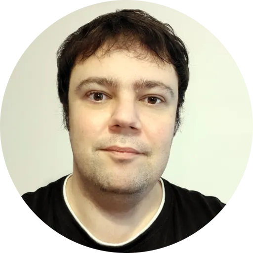 A circular-cropped photo of Mihai's face. Mihai has short dark hair, is wearing a black T-shirt and smiling slightly.